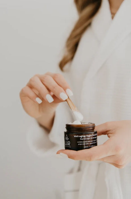 Vrouw in witte badjas brengt veganistische gezichtscrème, huidverzorgings- en wellnessproducten aan.