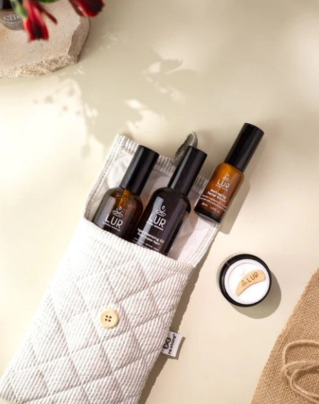 Diverse massageoliën en balsems in amberkleurige flesjes, gerangschikt in een stoffen zakje op een lichte ondergrond.