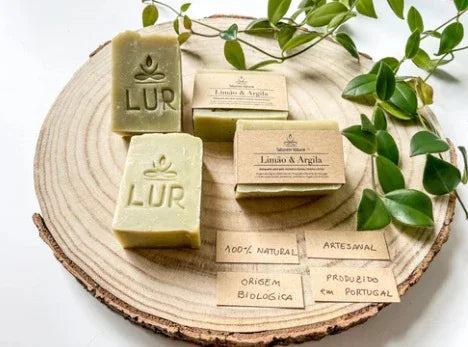 Handgemaakte natuurlijke zepen met groene bladeren op een houten frame, biologisch gecertificeerd en gemaakt in Portugal.