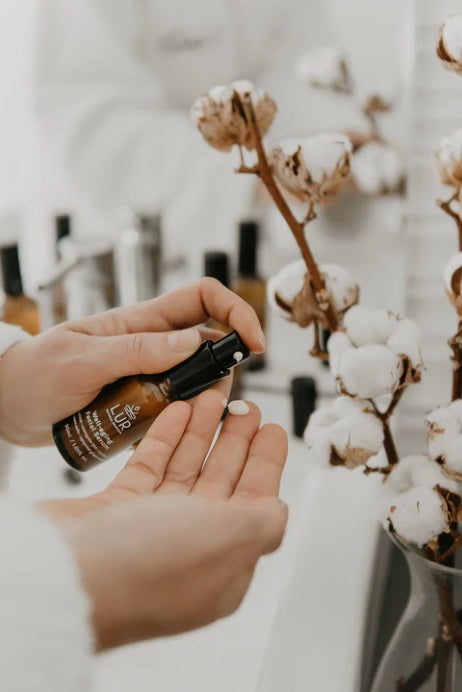 Hand brengt massageolie aan naast een katoenplant in een spa- en wellnessomgeving.