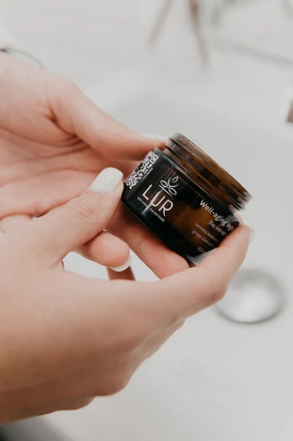 Handen die een amberkleurige pot met gezichtscrème vasthouden in een badkamer.