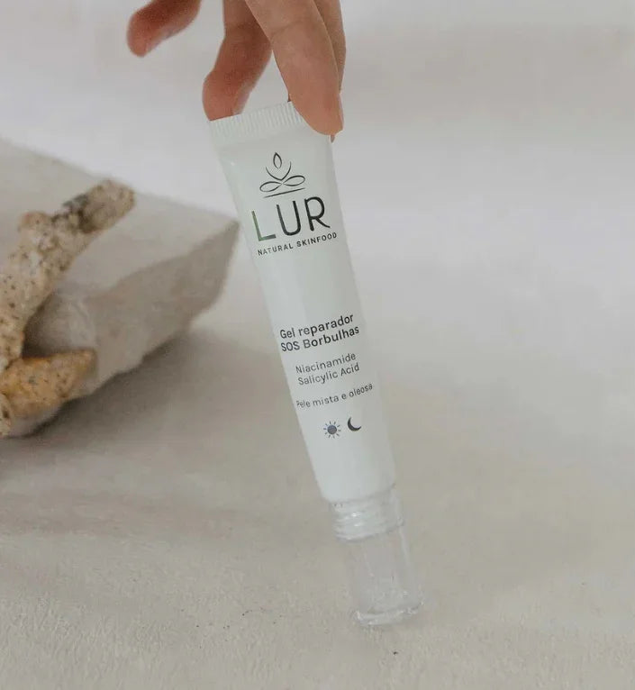 Hand die LUR Natural Skinfood SOS gel met niacinamide en salicylzuur op een stenen oppervlak vasthoudt.