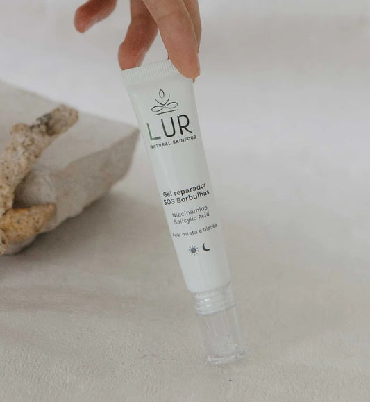 Hand die LUR Natural Skinfood SOS gel met niacinamide en salicylzuur op een stenen oppervlak vasthoudt.