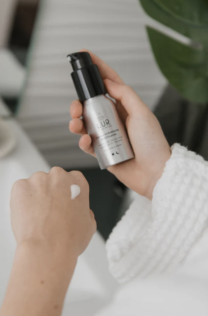 Hand die een hydraterend serum aanbrengt vanuit een zilverkleurige pompflacon, onderdeel van de huidverzorgingsroutine.